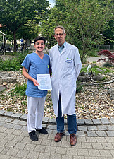 Nico Englisch (Pflegekraft im medbo Zentrum für neurologische Reha, Station 24b) erhält Urkunde von Prof. Schlachetzki im Außenbereich des medbo Bezirksklinikums.