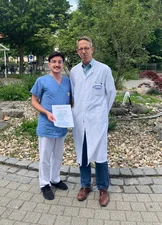 Nico Englisch (Pflegekraft im medbo Zentrum für neurologische Reha, Station 24b) erhält Urkunde von Prof. Schlachetzki im Außenbereich des medbo Bezirksklinikums.