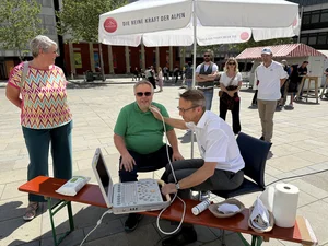 Arzt untersucht bei öffentlicher Aktion auf dem Neupfarrplatz die Halsschlagader eines Mannes per Ultraschall, mehrere Passanten schauen zu.