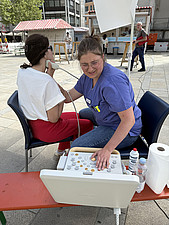Pflegekraft untersucht Besucherin am Infostand per Ultraschall – Marktstände im Hintergrund.