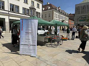 Infostand der Schlaganfall-Initiative mit Zelt, Roll-Up und Fahrrad auf dem Regensburger Neupfarrplatz.